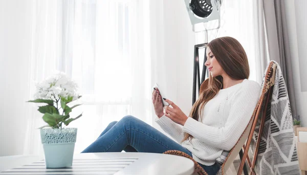 Frau sitzt zu Hause auf modernem Stuhl und nutzt Tablet-Computer, entspannt im Wohnzimmer — Stockfoto