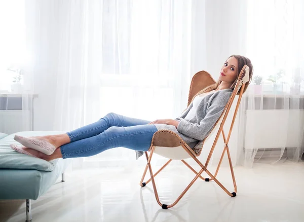 Vrouw thuis zit op moderne stoel in de buurt van venster ontspannen in woonkamer — Stockfoto