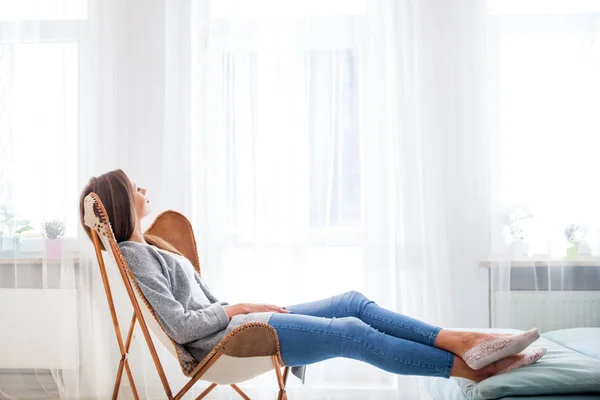 Frau sitzt zu Hause auf modernem Stuhl am Fenster und entspannt sich im Wohnzimmer — Stockfoto