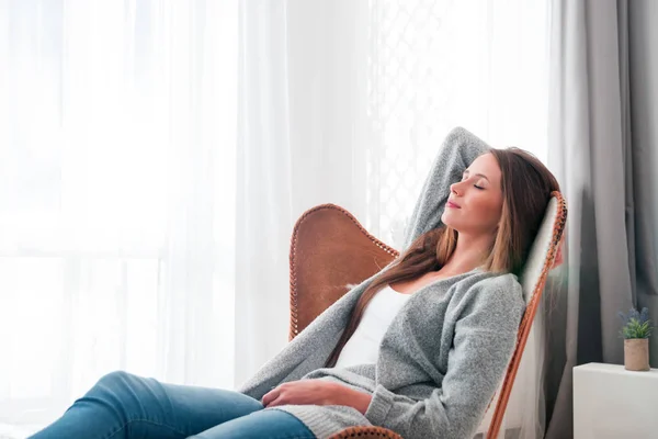 Vrouw thuis zit op moderne stoel in de buurt van venster ontspannen in woonkamer — Stockfoto