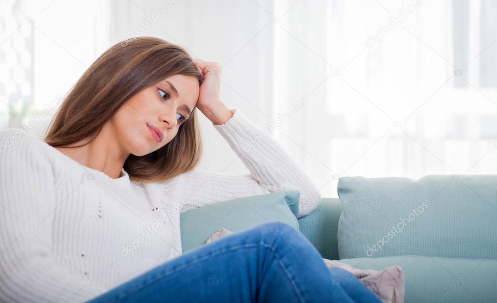 Sad woman sitting on sofa at home deep in thoughts, thinking about important things