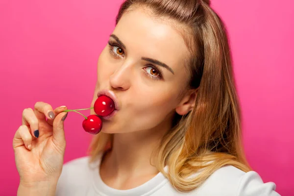 Woman over pink background eating cherry fruit — Stock Photo, Image