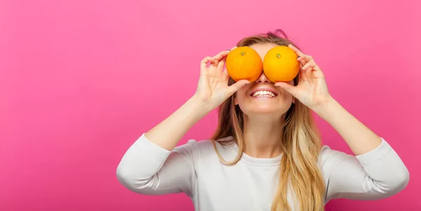 Meisje met twee oranje vruchten op roze achtergrond — Stockfoto