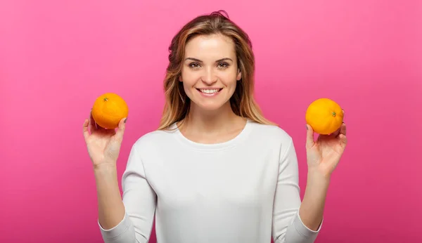 Flicka med två orange frukter på rosa bakgrund — Stockfoto