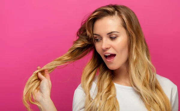 Mooie blonde op roze achtergrond meisje kijkend naar haar lange haren — Stockfoto