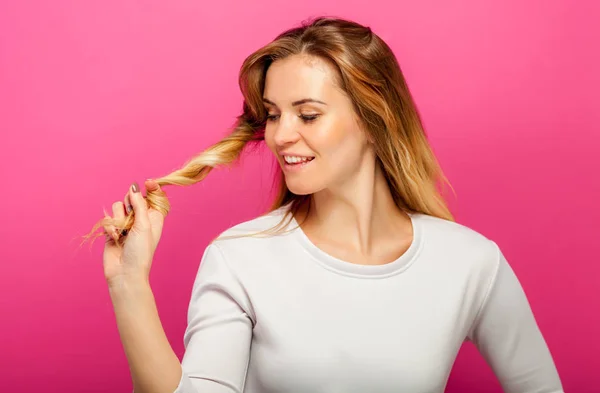 Beautiful blonde on pink background girl looking at her long hair — Stock Photo, Image