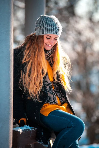 冬公園の木製フェンスの上に座っている若い女性 — ストック写真