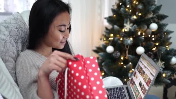 快乐的亚洲女孩坐在装饰过的圣诞树旁 带着笔记本电脑在网上购物 — 图库视频影像