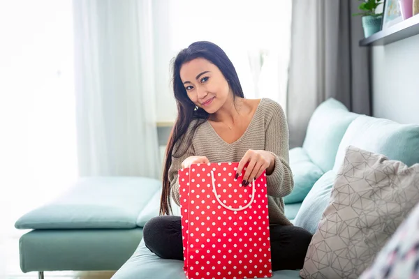 Mujer asiática en casa sosteniendo bolsa de regalo roja mirando a la cámara —  Fotos de Stock
