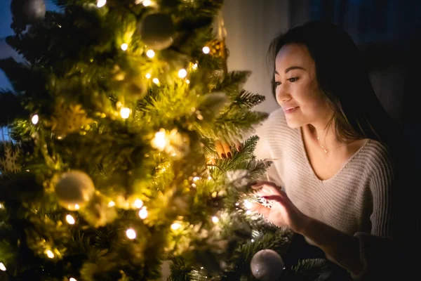 Beautiful Asian woman decorating Christmas tree in home at evening — ストック写真