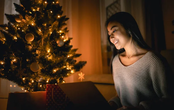 Happy asian girl shopping online with laptop sitting near decorated christmas tree background at evening — ストック写真