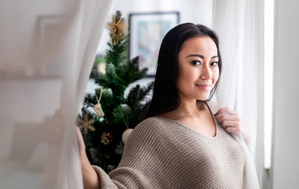 Gelukkig aziatische vrouw staan in de buurt venster in kerst versierd huis — Stockfoto