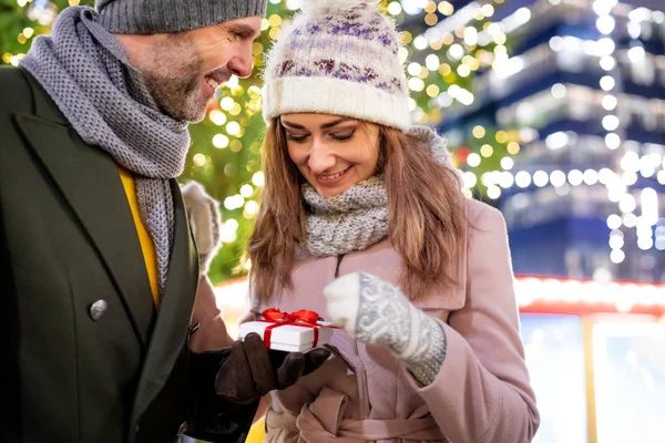 Das Paar verschenkt Weihnachtsgeschenke vor dem Hintergrund der Außendekoration bei einem Abendspaziergang — Stockfoto