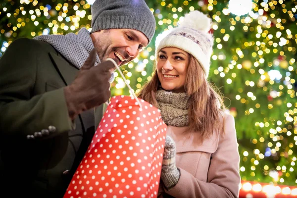 Das Paar verschenkt Weihnachtsgeschenke vor dem Hintergrund der Außendekoration bei einem Abendspaziergang — Stockfoto