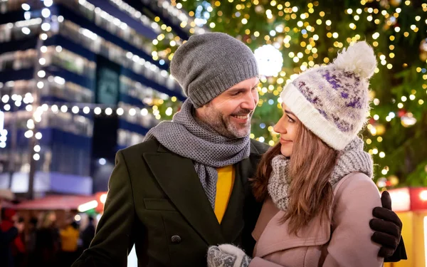 Casal amoroso no fundo de férias de inverno decorações durante uma caminhada à noite em torno da feira de Natal — Fotografia de Stock