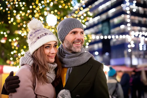 Casal amoroso no fundo de férias de inverno decorações durante uma caminhada à noite em torno da feira de Natal — Fotografia de Stock