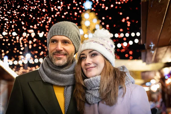 Casal amoroso no fundo de férias de inverno decorações durante uma caminhada à noite em torno da feira de Natal — Fotografia de Stock