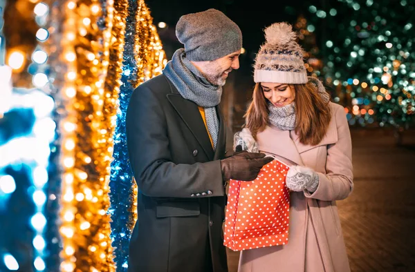 Casal com um presente de Natal depois de fazer compras anda em uma rua decorada — Fotografia de Stock