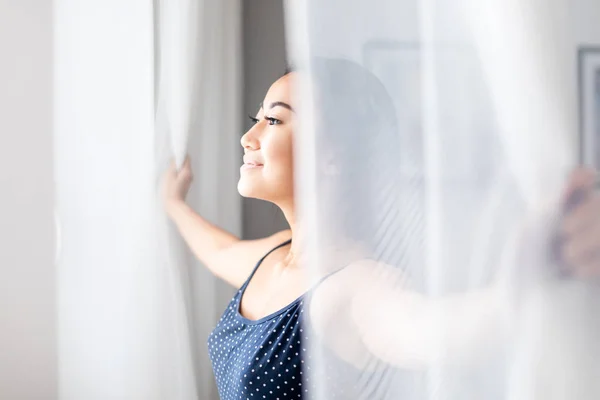 Asian girl wearing pajamas open window lace curtains in home at morning — Stock Photo, Image
