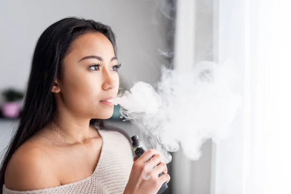 Lässige asiatische Frau verdampft elektronische Zigarette zu Hause — Stockfoto