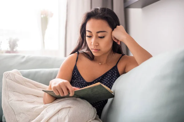 Konzentrierte asiatische Mädchen liegen auf dem Sofa und lesen ein Buch zu Hause — Stockfoto