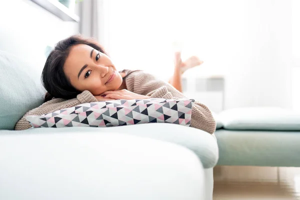 Boldog ázsiai lány feküdt a kanapén párnával otthon — Stock Fotó