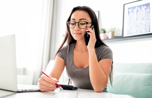 Asian woman using smartphone app and laptop for calaulating home budget finance taxes 로열티 프리 스톡 사진