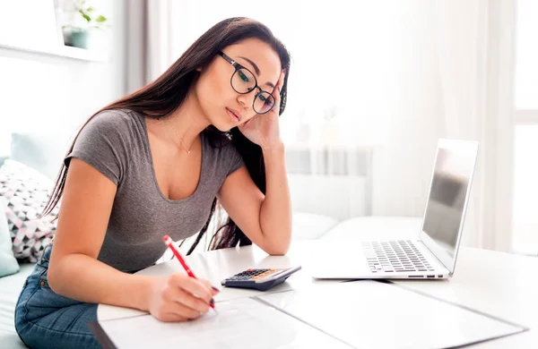 Wanhopige en bezorgde Aziatische vrouw die thuis belastingrekeningen berekent Stockfoto