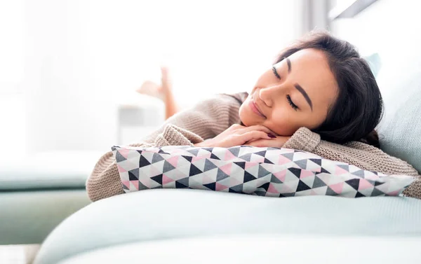 Happy asian girl lying on sofa with pillow at home Stock Photo