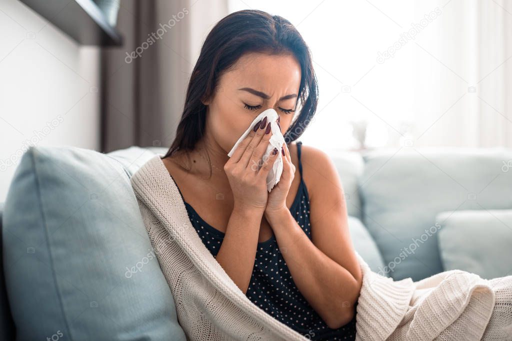 Asian girl suffering from cold sitting on bed at home