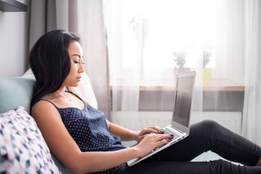 Evde kanepede dizüstü bilgisayar kullanan rahat Asyalı kız.