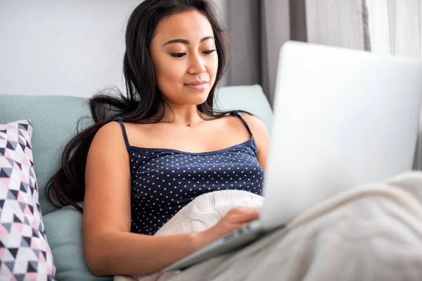 Relajado asiático chica usando laptop sentado en sofá en casa —  Fotos de Stock