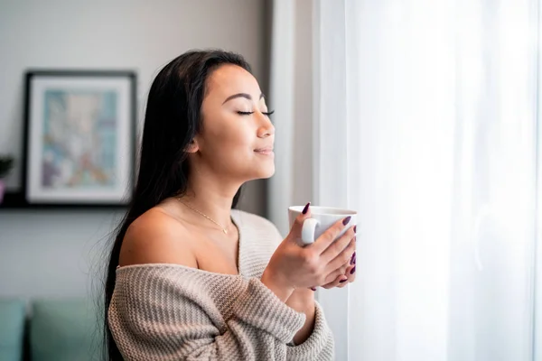 Rahatlamış Asyalı kadın bir fincan çayla ya da kahve içerek evde vakit geçiriyor. — Stok fotoğraf