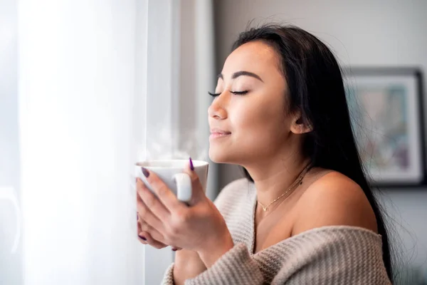 Relaxed asian woman with cup of tea or coffee spending leisure time at home — Stock Photo, Image