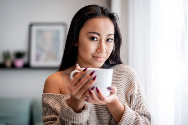 Relaxed asian woman with cup of tea or coffee spending leisure time at home — Stock Photo, Image