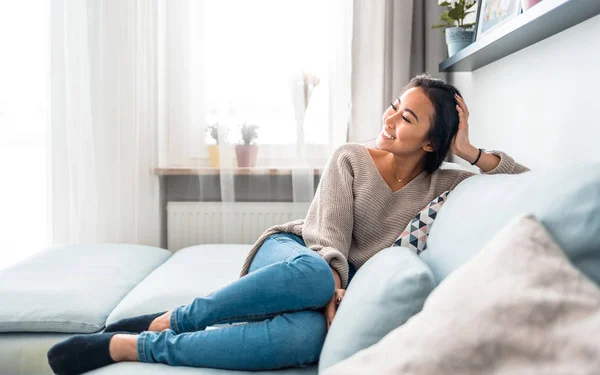 Entspannt lächelnd asiatische Frau sitzt auf Sofa zu Hause — Stockfoto