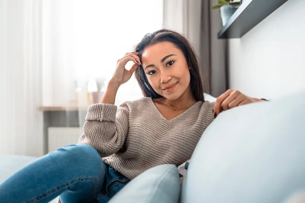 Entspannt lächelnd asiatische Frau sitzt auf Sofa zu Hause — Stockfoto