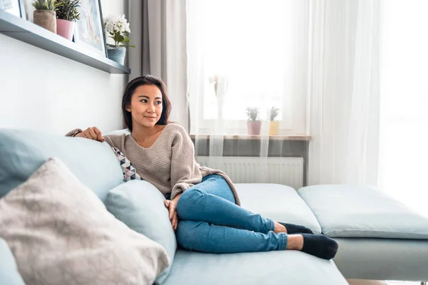 Entspannt lächelnd asiatische Frau sitzt auf Sofa zu Hause — Stockfoto