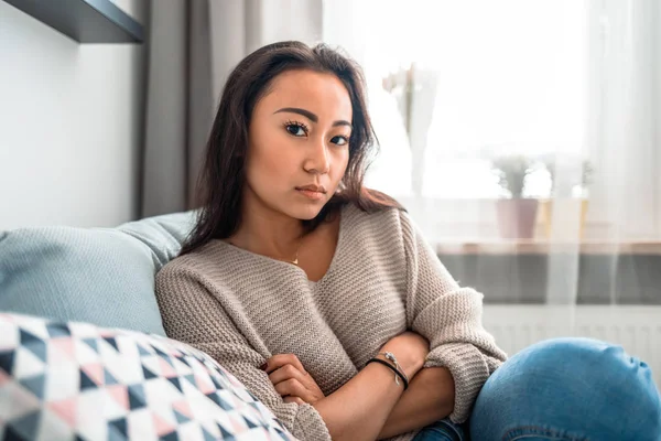 Sad asian girl sitting on sofa at home and thinking — Stock Photo, Image