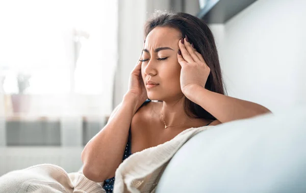 Upset depressed asian girl on couch suffering from headache migraine — Stock Photo, Image