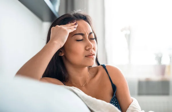 Molesto deprimido asiático chica en sofá sufrimiento de dolor de cabeza migraña —  Fotos de Stock