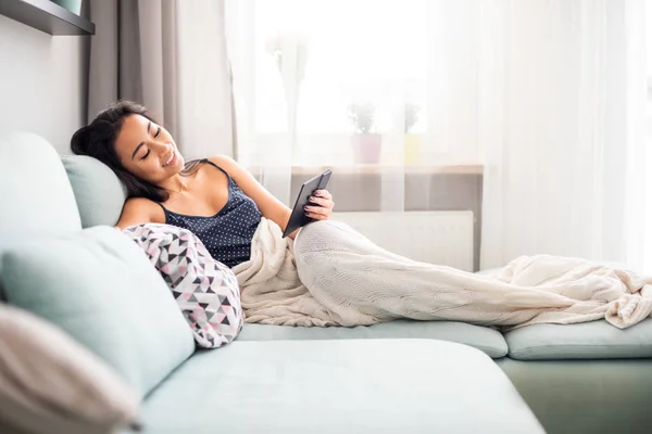 Mladá asijská žena sedí na pohovce pomocí čtečky tablet a čtení ebook doma — Stock fotografie