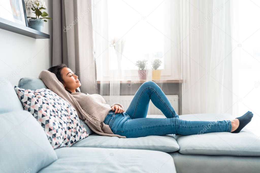 Relaxed smiling asian woman sitting on sofa at home