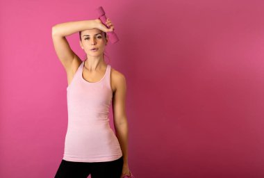 Pembe arka planda aptal gibi duran genç ve fit bir kadın.