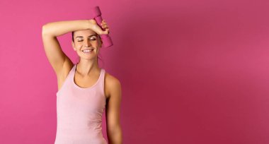 Pembe arka planda aptal gibi duran genç ve fit bir kadın.