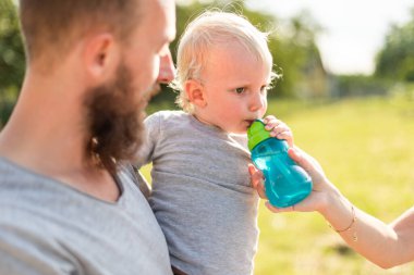 Çocuk ve ailesi dışarıda yürürken şişeden su içiyorlar.