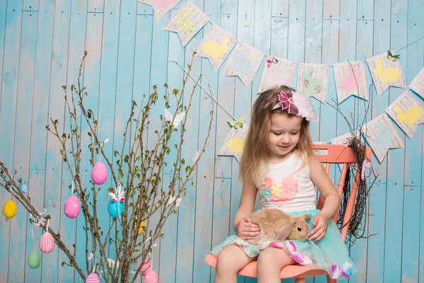 Pequeña hermana hermosa y encantadora chica junto con el conejo sentado en el suelo o silla en ropa azul brillante Pascua, huevos, humor festivo, emoción y sonrisa fiesta sorpresa celebración —  Fotos de Stock
