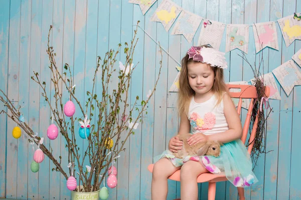 Pequena irmã menina bonita e encantadora, juntamente com o coelho sentado no chão ou cadeira em roupas azuis brilhantes Páscoa, ovos, humor festivo, emoção e sorrir celebração de férias surpresa — Fotografia de Stock
