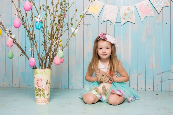 Little beautiful and charming girl sister along with rabbit sitting on the floor or chair in bright blue clothes Easter, eggs, festive mood, emotion and smile surprise holiday celebration — Stock Photo, Image