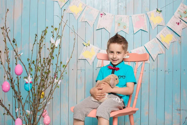 Niño pequeño hermano junto con conejo sentado en el suelo o silla en ropa azul brillante Pascua, huevos, humor festivo, emoción y sonrisa fiesta sorpresa celebración —  Fotos de Stock